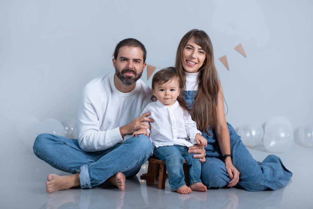 A joyful family portrait with parents and child in casual denim, surrounded by balloons.